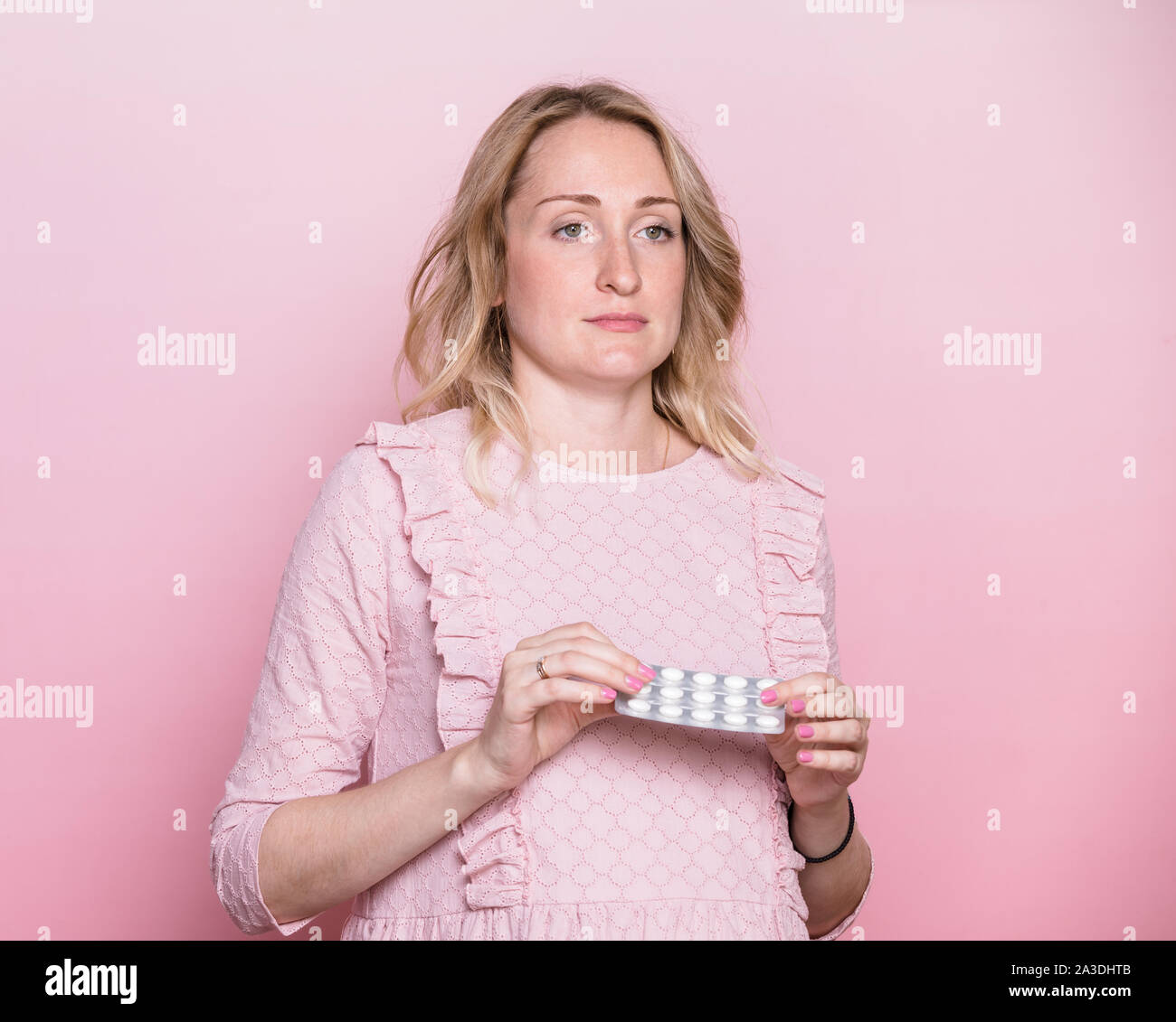 Giovane donna incinta indossando abiti rosa azienda blister di medicina compresse medita di prendere pillole durante la gravidanza o non. Studio shot in rosa ba Foto Stock