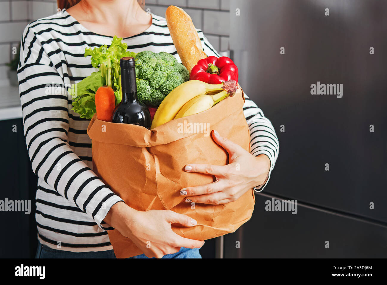 Donna in piedi nella sua cucina e tenendo un sacco pieno di prodotti Foto Stock