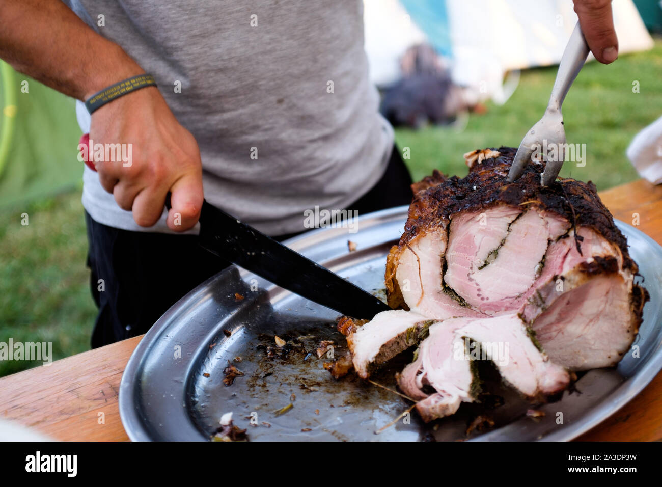 Uomo taglio in fette una deliziosa porchetta, italiano tradizionale cibo di strada Foto Stock