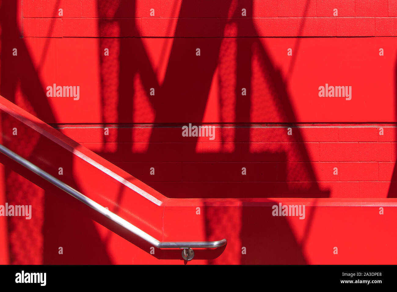 Rosso brillante scala di cemento e a parete in acciaio inox Ringhiera anteriore di un rosso corrispondente blocco di calcestruzzo parete con ombre astratte e lo spazio negativo Foto Stock