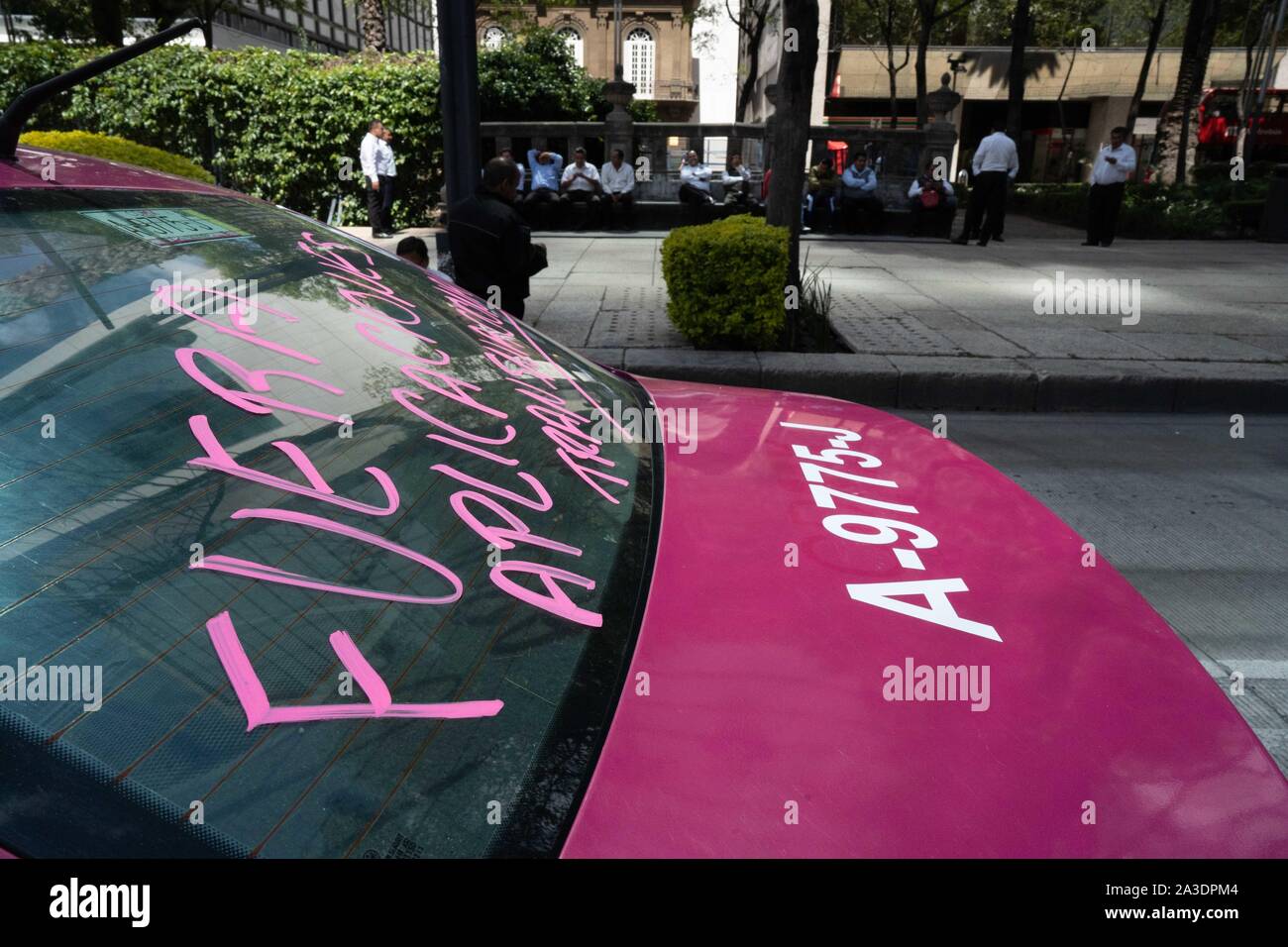 Migliaia di taxi sono visto parcheggiata sulle strade intorno alla statua dell'Angelo di indipendenza di Città del Messico. Slogan sul parabrezza leggere ÔFuera Aplicacion transnacionalesÕ (richiedendo la rimozione di applicazioni straniere). I conducenti di taxi può essere visto in appoggio in ombra in background. Photo credit: Lexie Harrison-Cripps Foto Stock