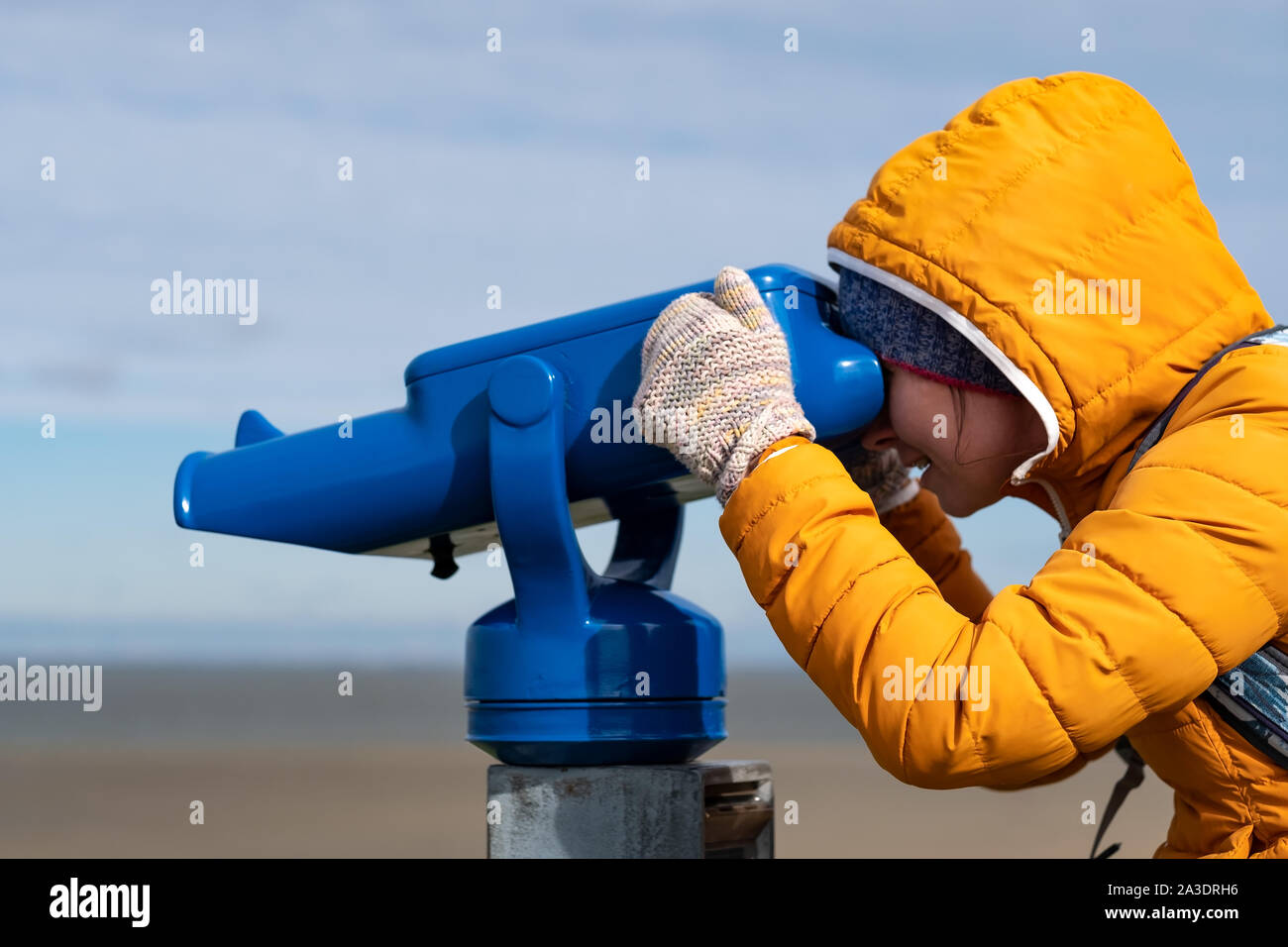 Donna in cappotto giallo guardando il mare utilizzando a gettone binocolo Foto Stock