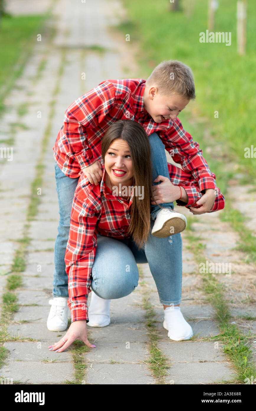 Mom con uno stupito espressione sul viso, rannicchiato, detiene una ridente figlio sulle sue spalle. Foto Stock