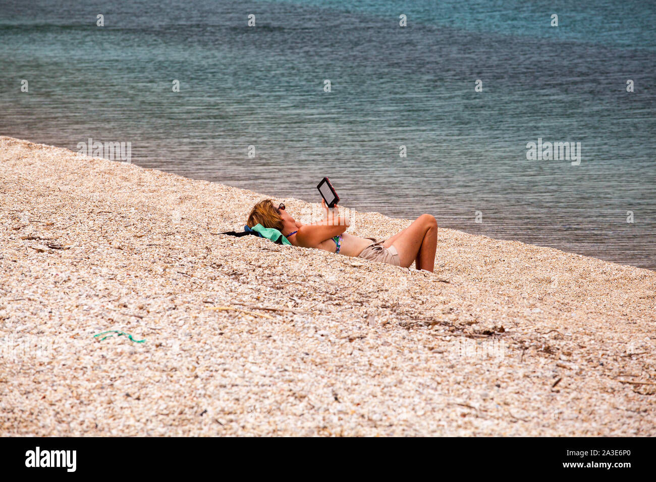 Donna sdraiata su una spiaggia di ciottoli la lettura di un libro di kindle reader Foto Stock