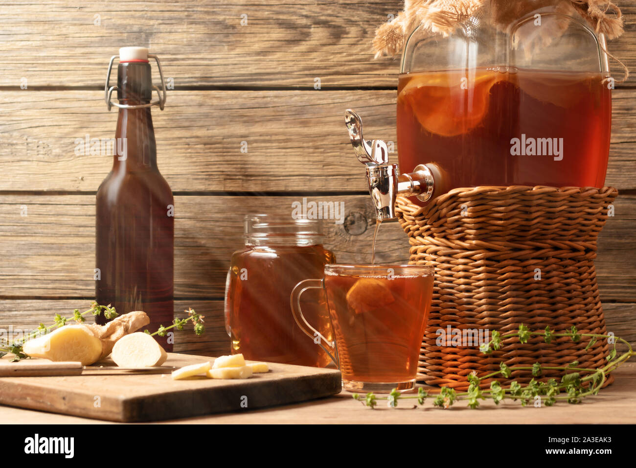 Freschi Fatti in casa il Kombucha tè fermentato drink nel vaso con rubinetto e in lattine-mug e cup su sfondo di legno. Foto Stock