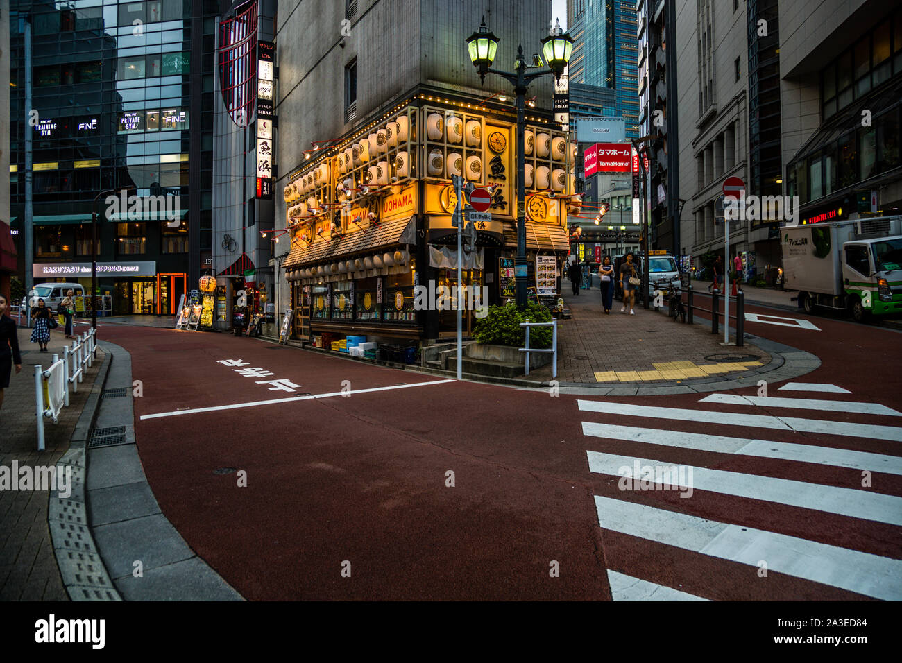 Il ristorante all'angolo Uohama, con le sue lanterne rotonde di carta, si trova in un angolo di strada tranquillo al crepuscolo tra la vita di strada di Tokyo, Giappone, un lampione doppio segna il bordo del marciapiede. Foto Stock