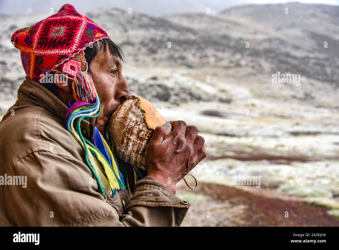 Un uomo Quechua in testa tradizionale colpi di usura su una conchiglia di accogliere i visitatori al Huampacocha lodge. Ausangate, Cusco, Perù Foto Stock