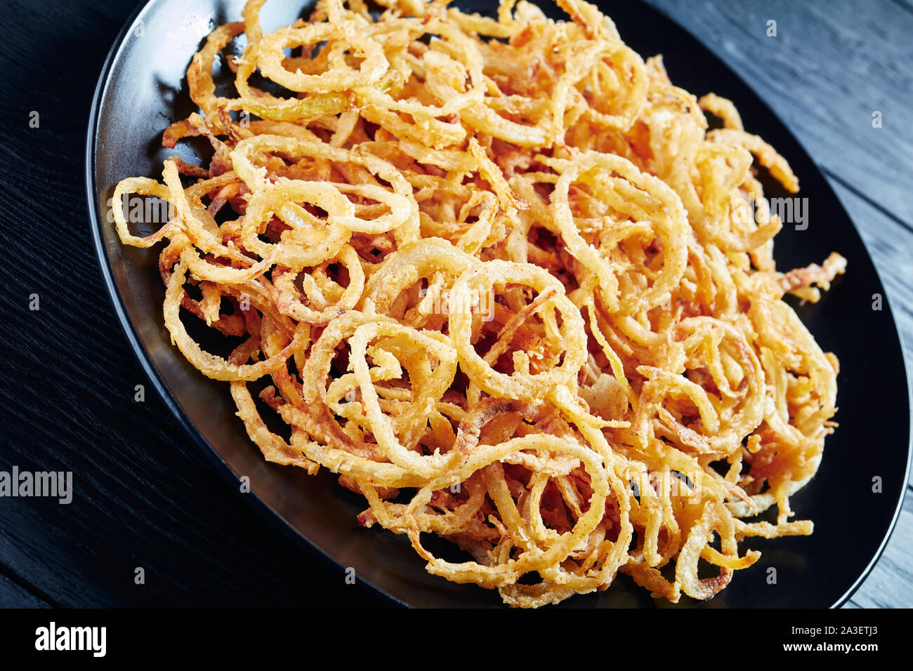 Close-up di francese croccante di cipolle fritte su una piastra nera su una tavola di legno, vista orizzontale dal di sopra, Foto Stock