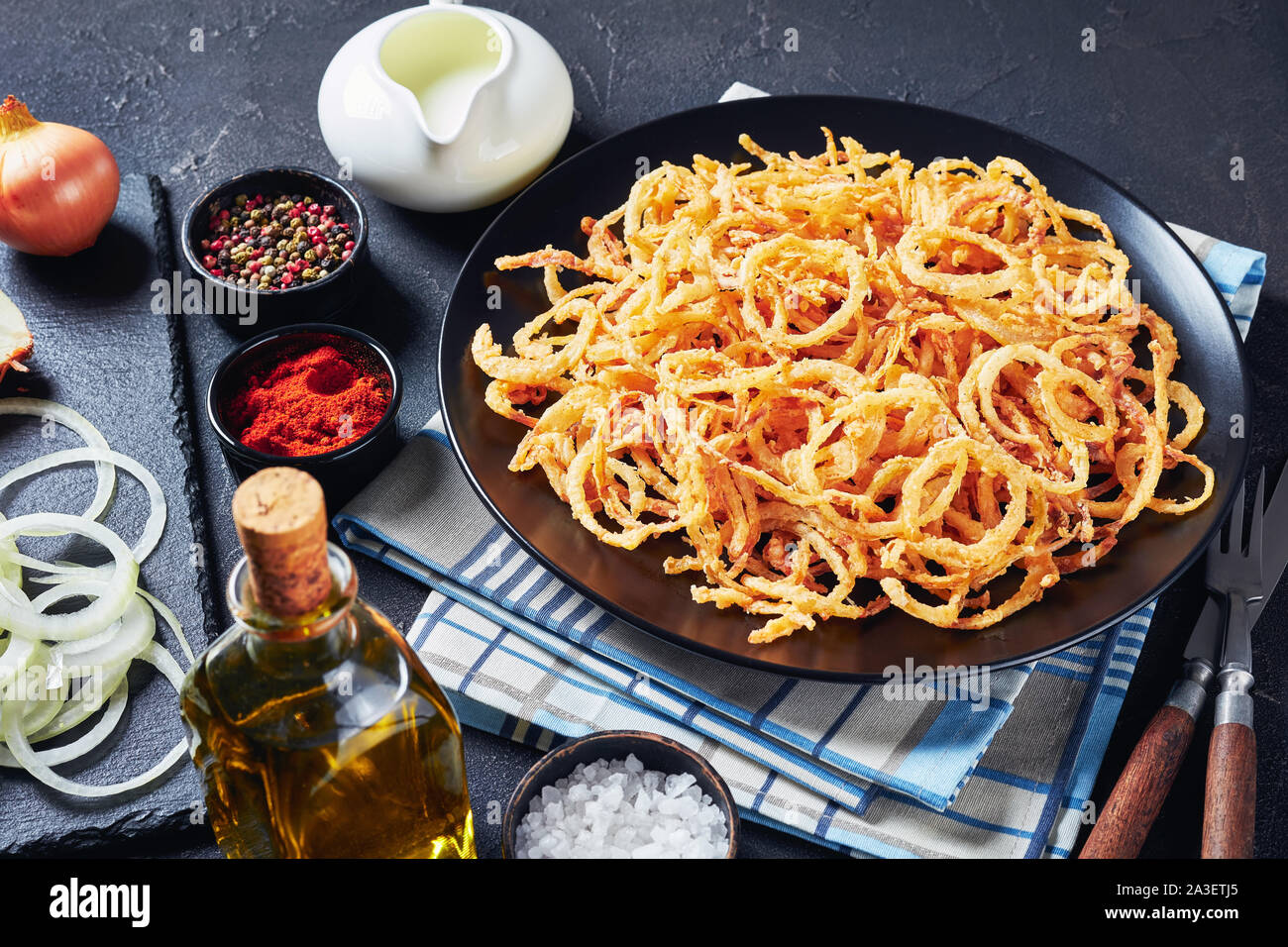 Il francese croccante di anelli di cipolla fritti e stringhe su una piastra nera su una tabella di calcestruzzo con ingredienti, orizzontale vista da sopra Foto Stock