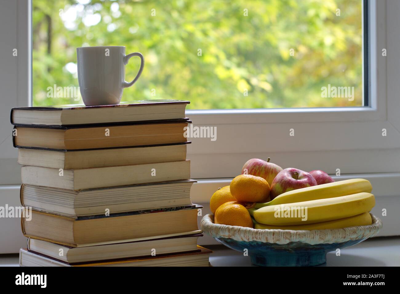 Libri e ciotola con frutti sul tavolo contro la finestra Foto Stock