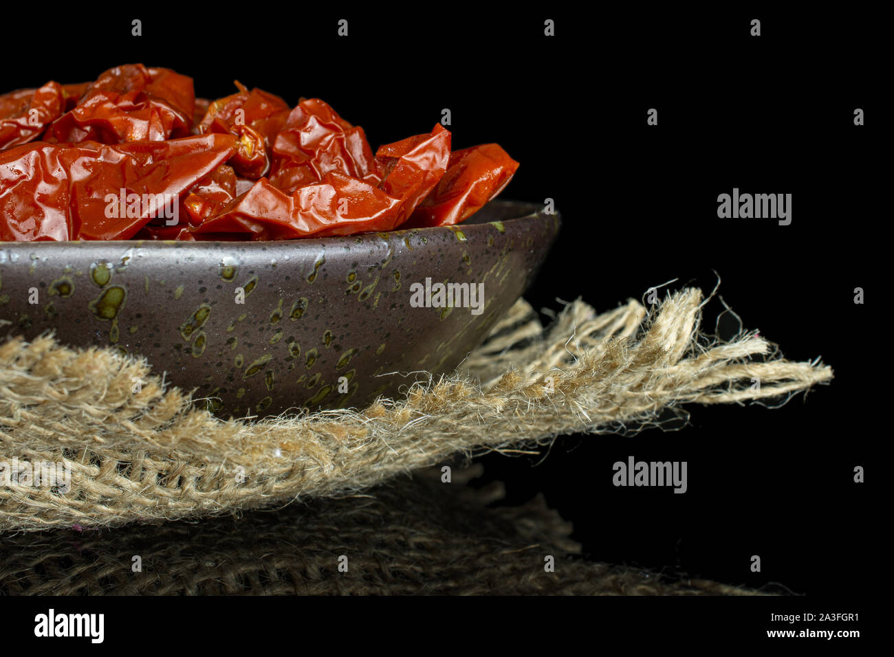 Sacco di fette di rosso secco pomodoro ciliegino closeup su grigio piastra ceramica sulla stoffa di iuta isolato sul vetro nero Foto Stock