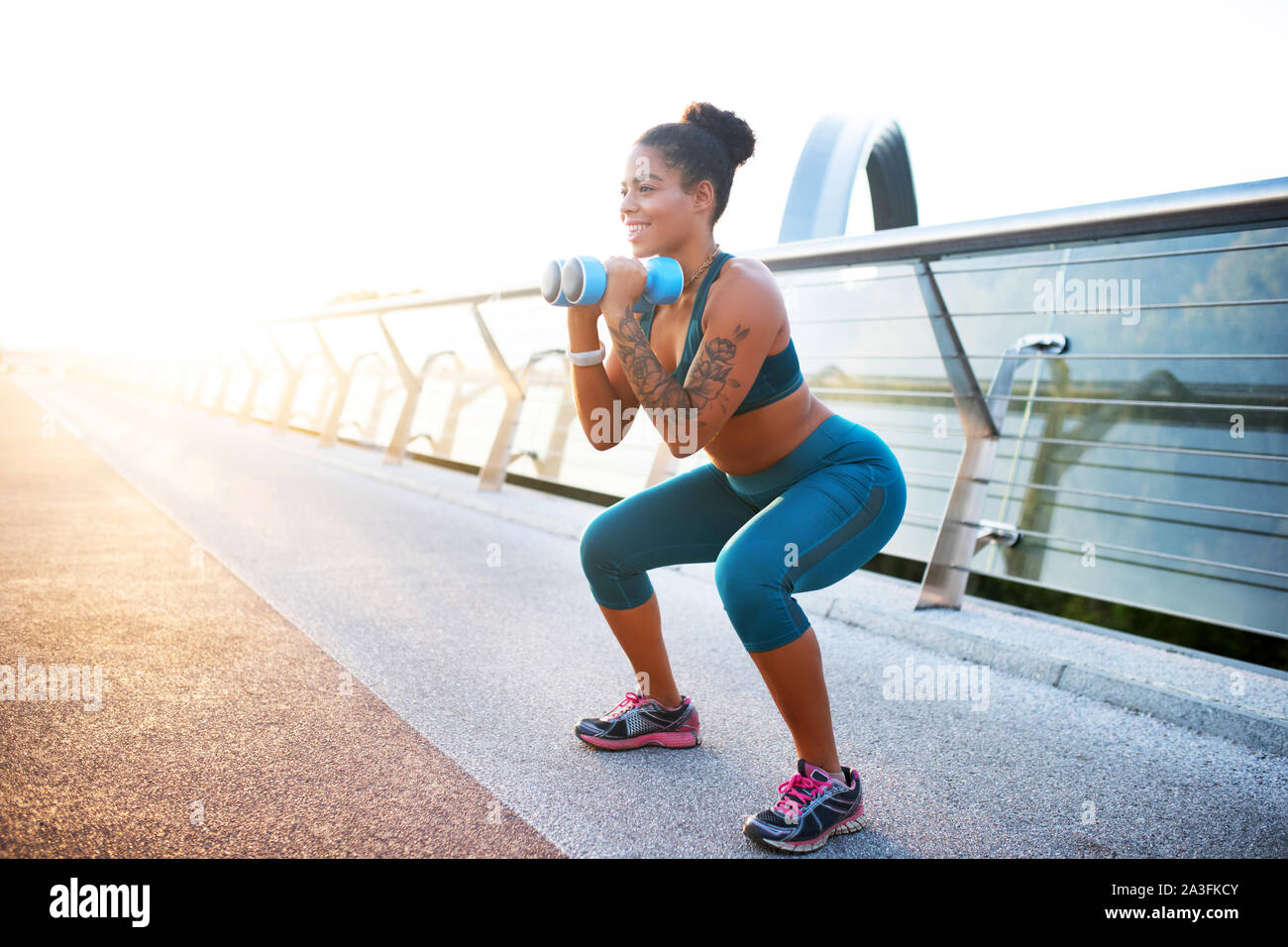 Sorridente donna tatuata facendo sit ups con barbells in armi Foto Stock