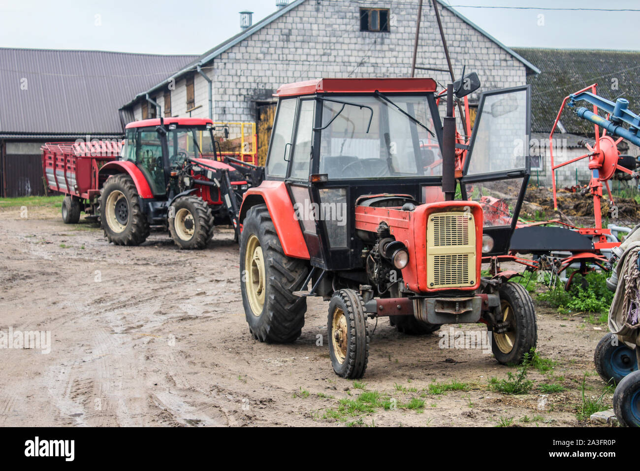 Red trattori e attrezzature agricole nel cortile di una fattoria di caseificio. Stalla in background. Podlasie, Polonia. Foto Stock