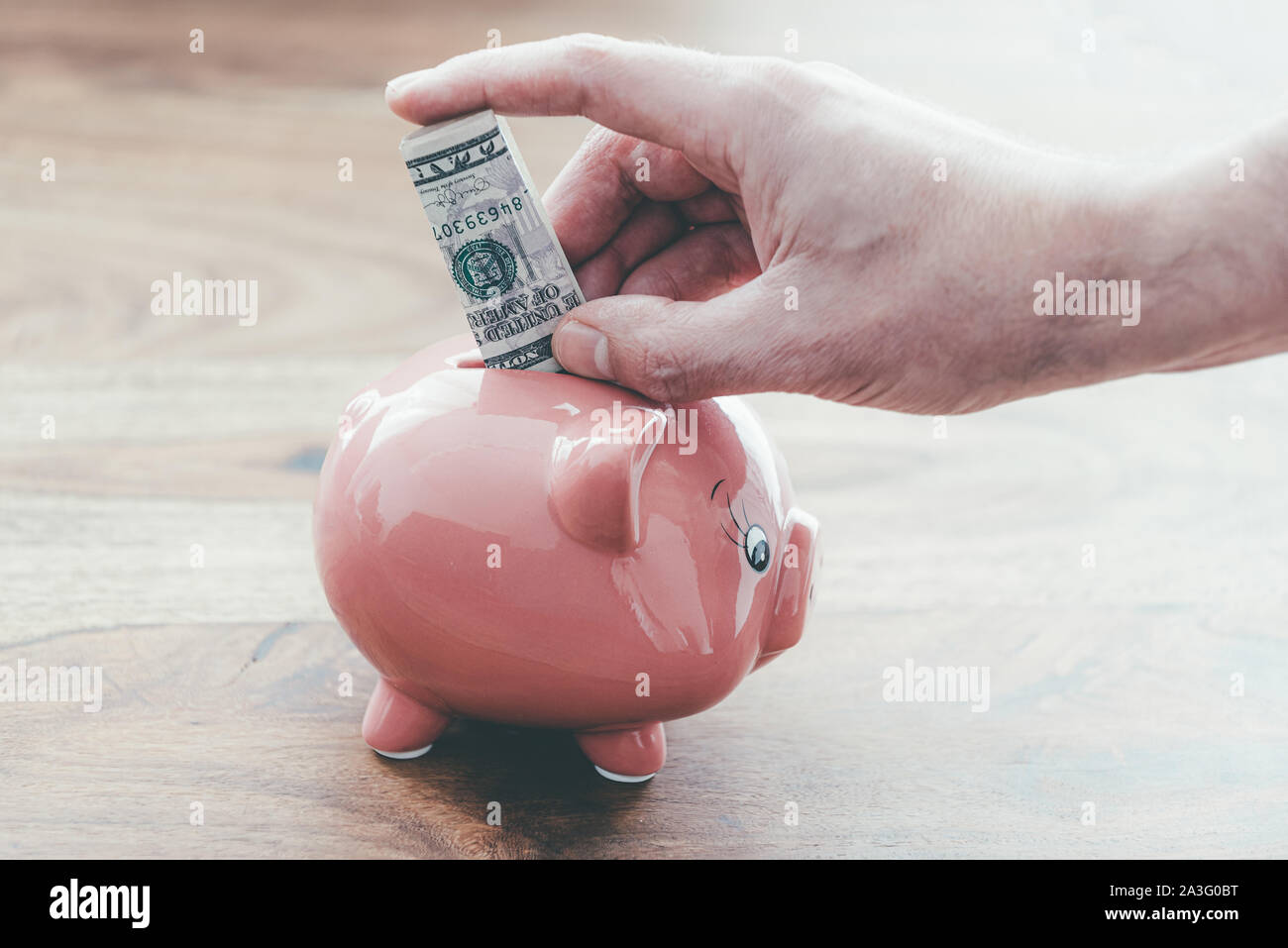 Close-up del maschio mettendo mano piegata dollaro in rosa salvadanaio sul tavolo di legno, home finanza e risparmio di denaro concept Foto Stock