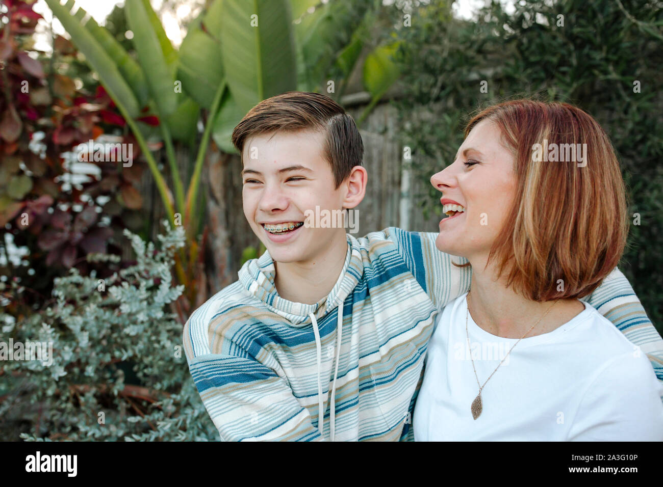Ridendo teen boy con bretelle abbracciando mid-40's mom Foto Stock