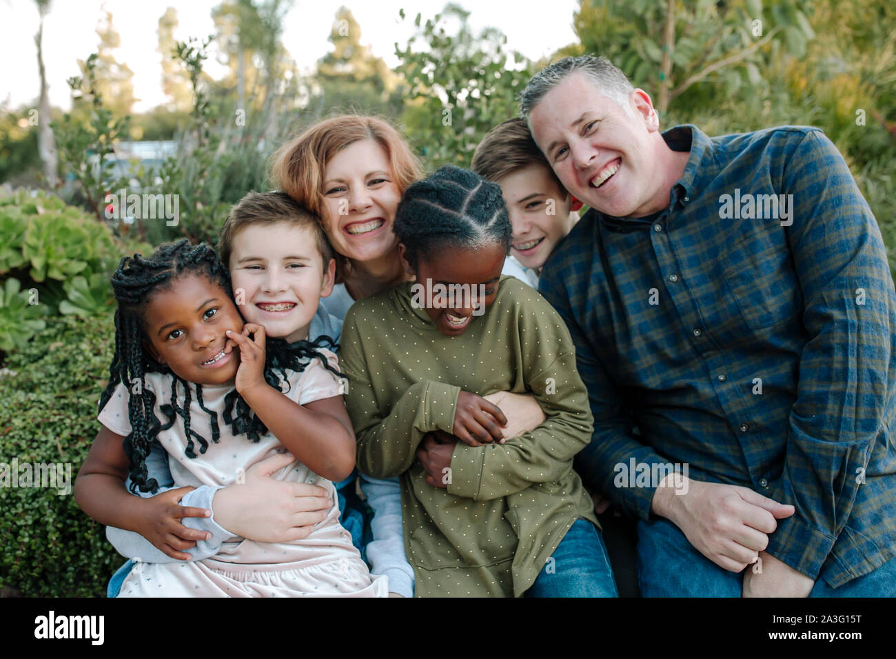 Gioiosa mixed-gara famiglia con quattro figli abbracciando all'aperto Foto Stock
