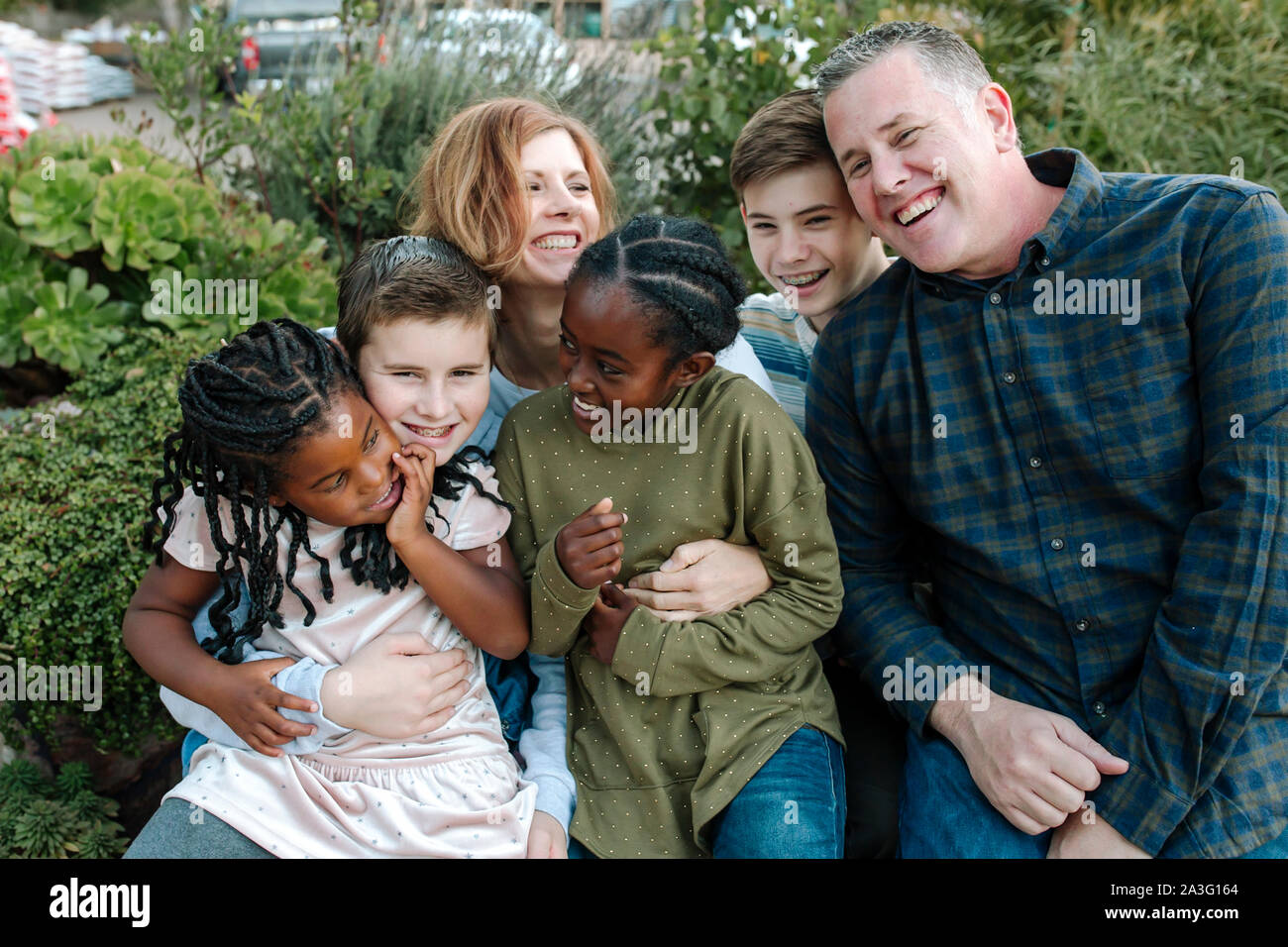 Ridendo gioiosa famiglia multirazziale all'aperto in un abbraccio di gruppo Foto Stock