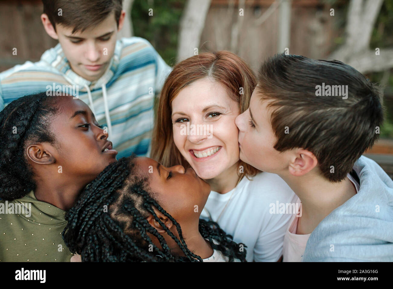 Sorridente mid-40's mom essendo abbracciato e baciato da multirazziale bambini Foto Stock
