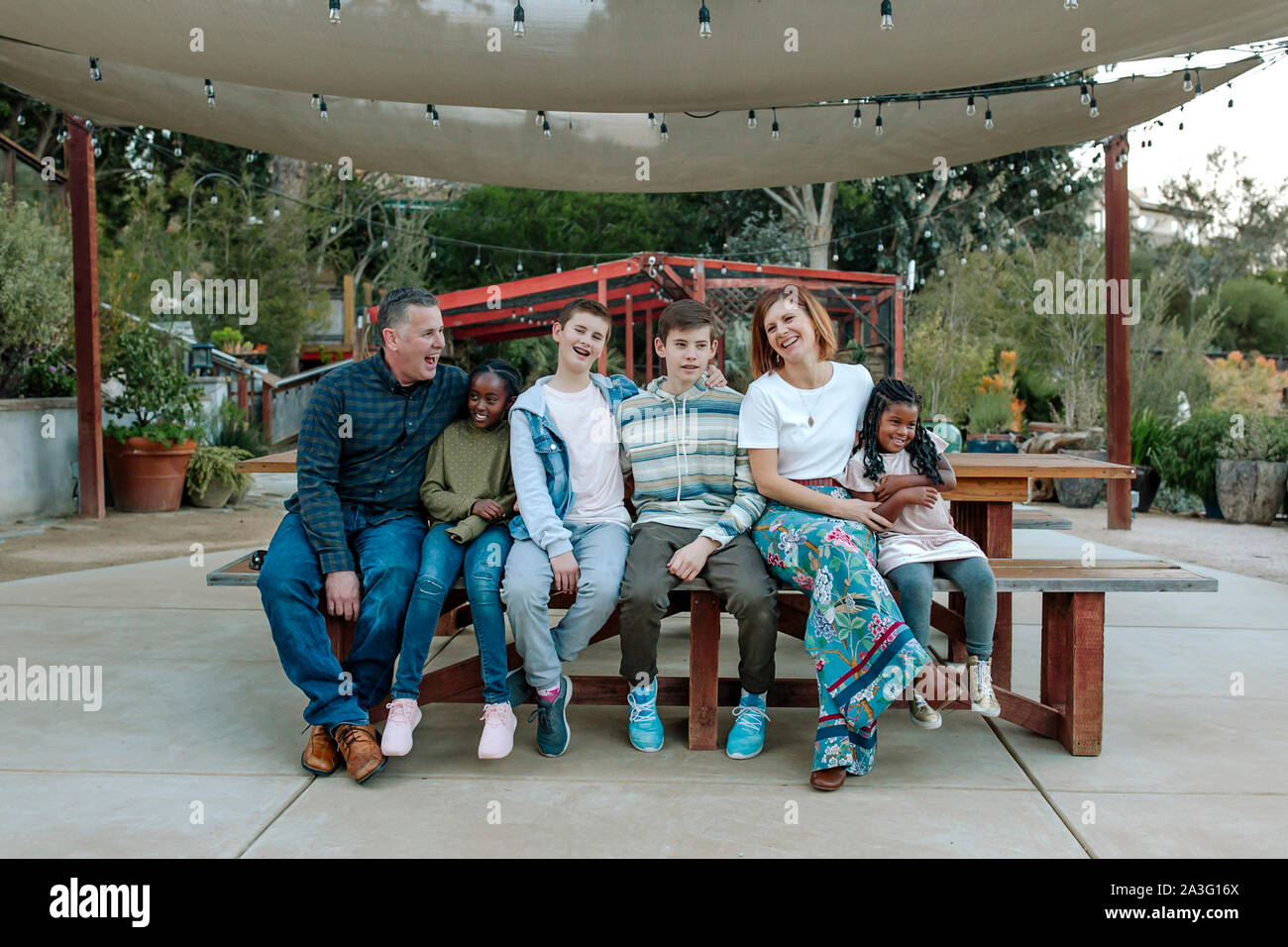 Ridendo multirazziale famiglia sul banco sotto il baldacchino del sole al vivaio Foto Stock