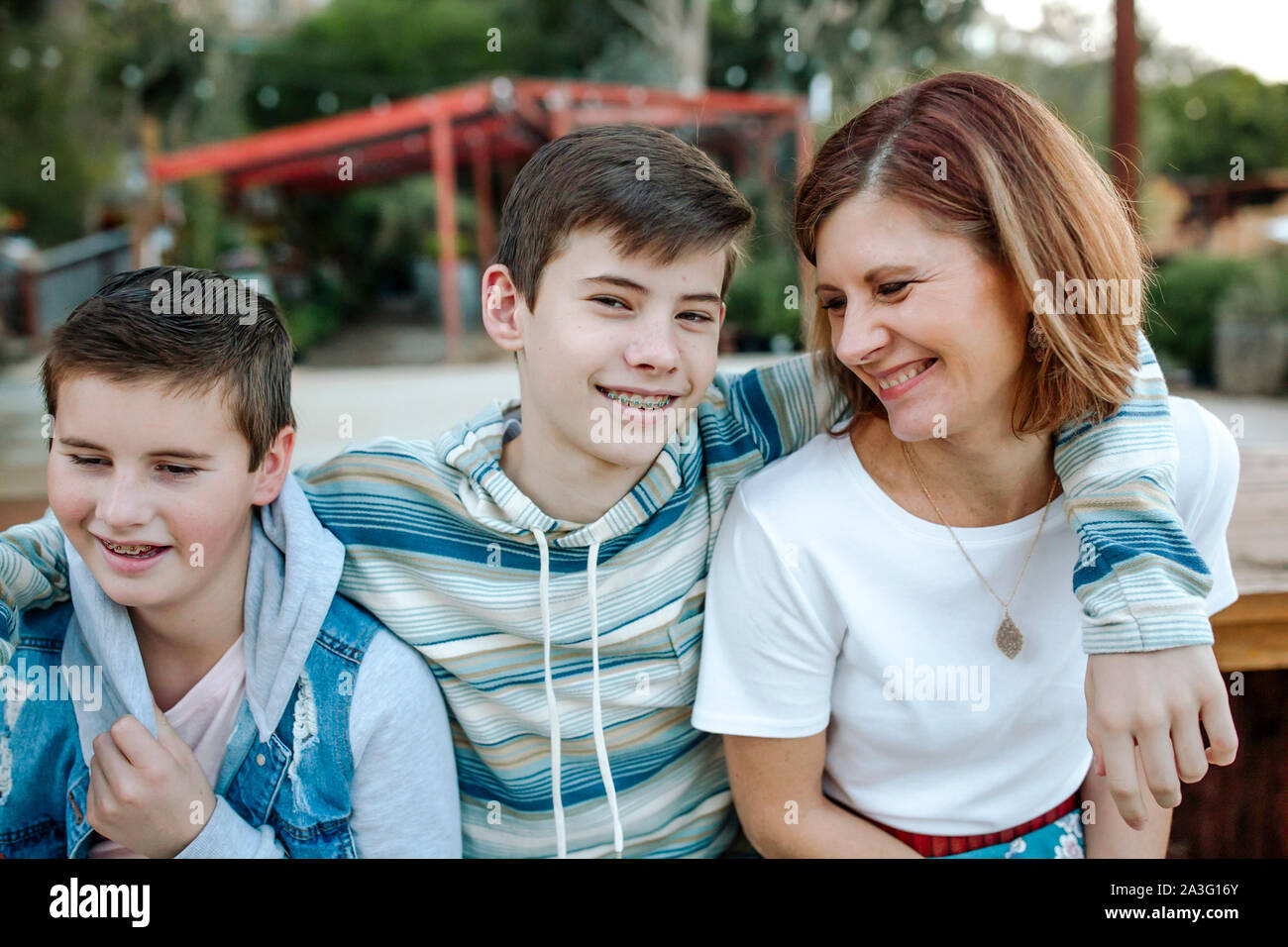 Sorridente teen boy con bretelle abbracci la mamma e il fratello più giovane Foto Stock