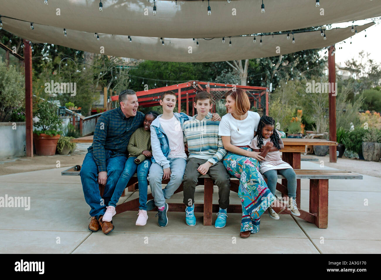 Gioiosa famiglia multirazziale ridere sul banco sotto ombrellone in vivaio Foto Stock
