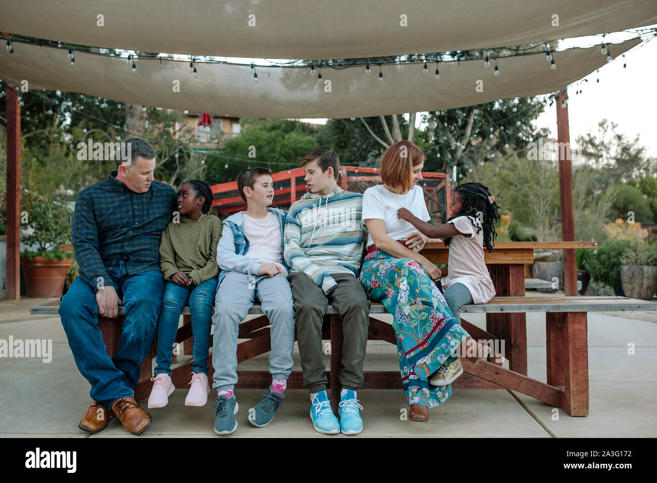 Famiglia multirazziale relax su una panchina sotto un bianco baldacchino del sole Foto Stock