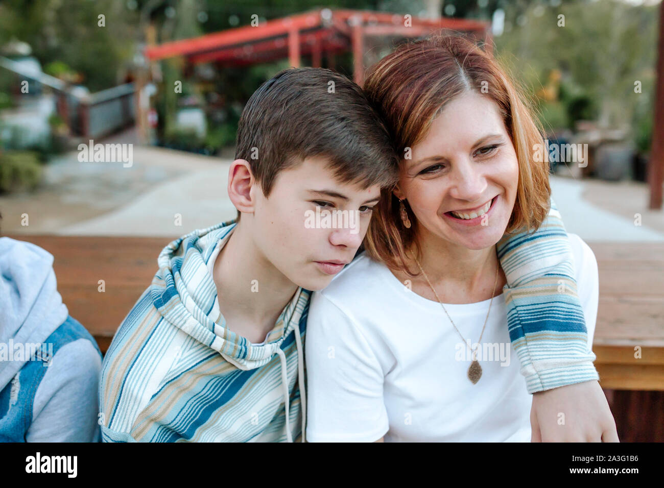 Gara teen figlio in blue striped shirt abbracciando sorridente mom Foto Stock