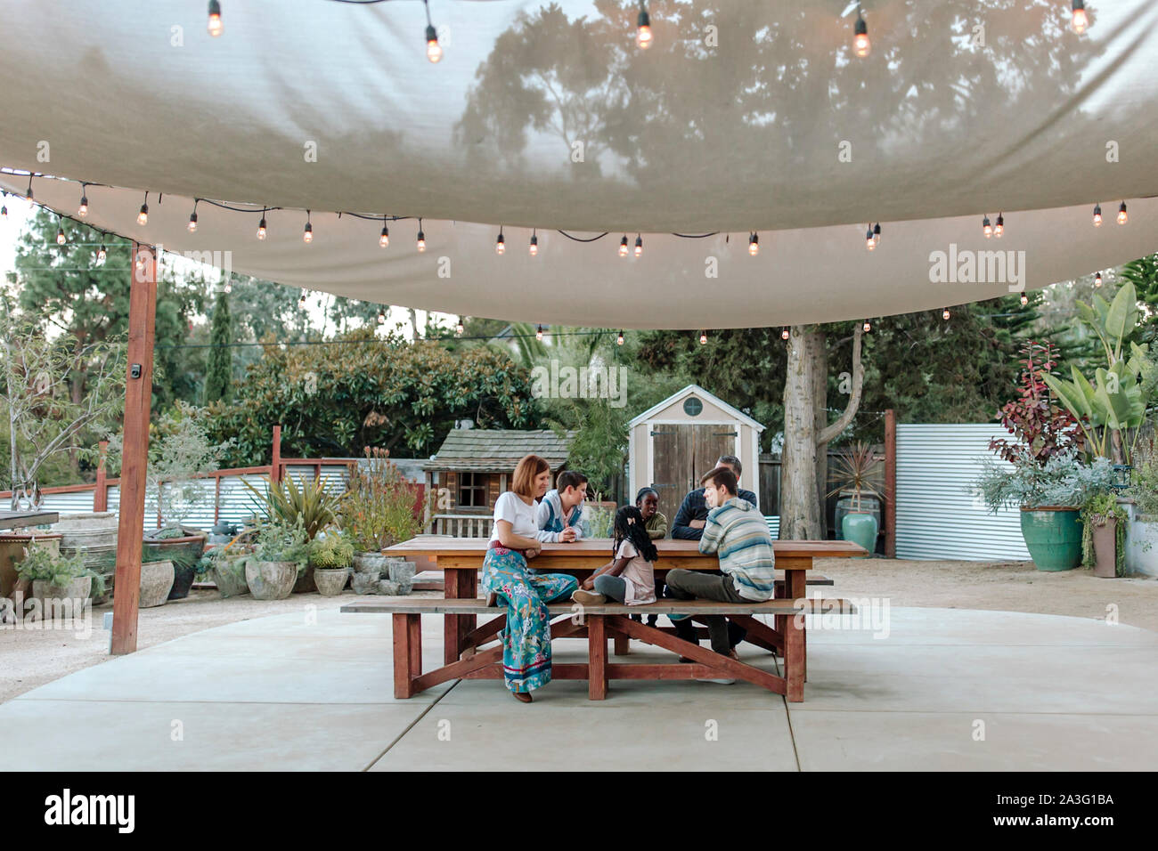Multirazziale famiglia al tavolo da picnic sotto il baldacchino del sole con luci di mercato Foto Stock