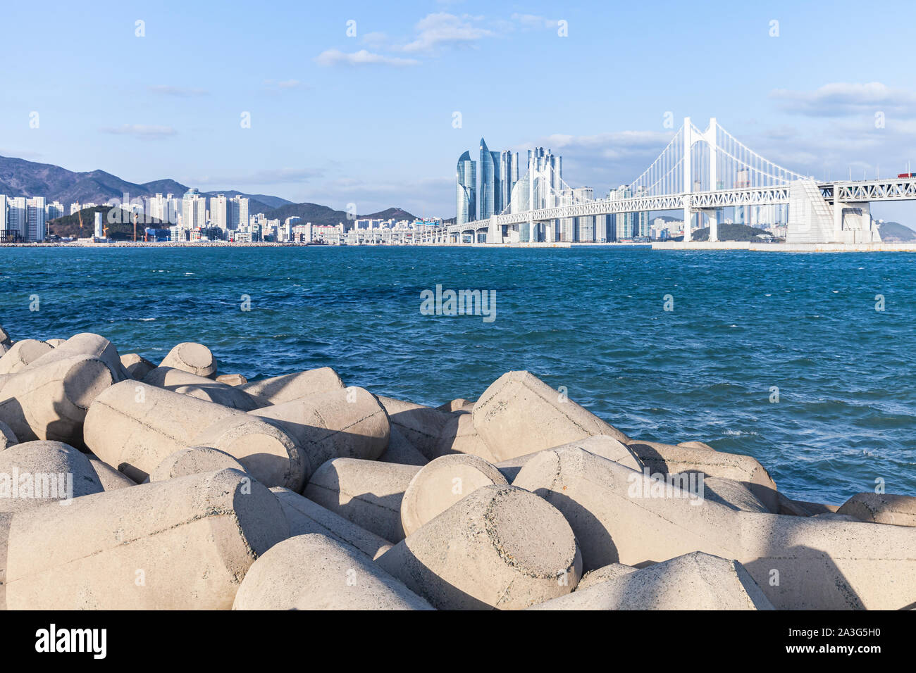 Corea del Sud. Paesaggio di Busan con calcestruzzo blocchi frangiflutti e la Gwangandaegyo o diamante ponte sullo sfondo Foto Stock