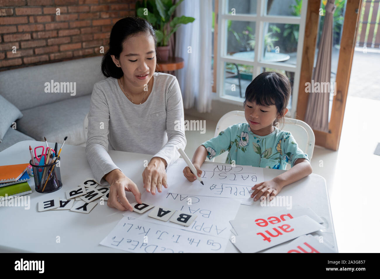 Madre e figlia di imparare a leggere e a scrivere una lettera a casa insieme. attività di homeschooling Foto Stock