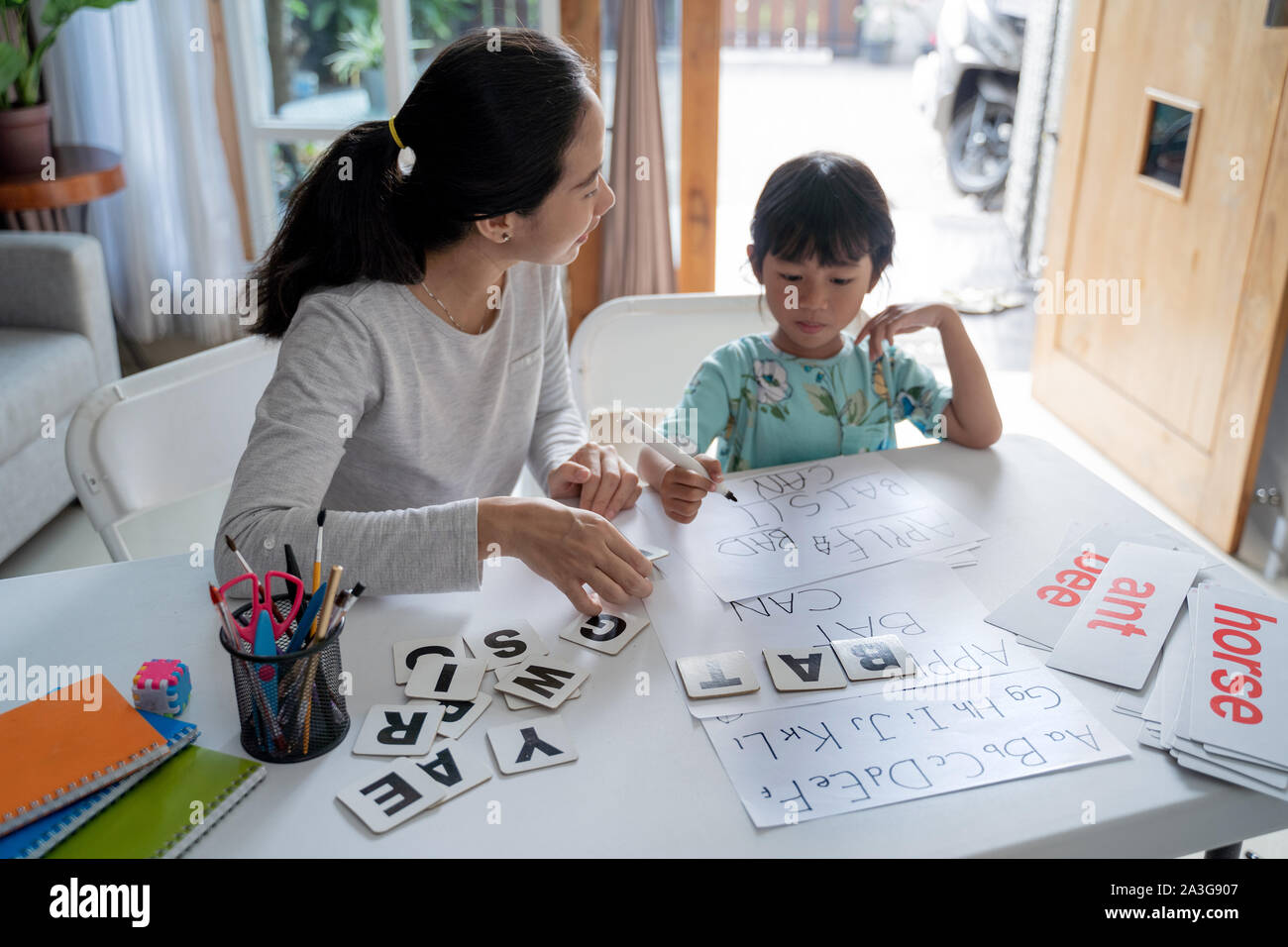 Madre e figlia di imparare a leggere e a scrivere una lettera a casa insieme. attività di homeschooling Foto Stock