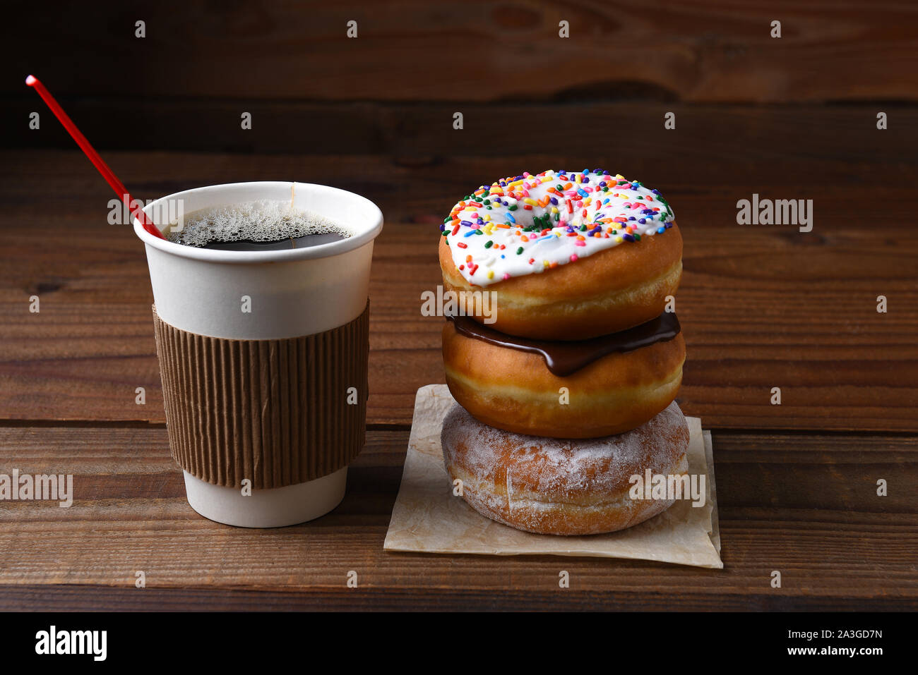 Un bicchiere di carta di caldo fresco preparato del caffè accanto a una pila di ciambelle di fantasia. Foto Stock