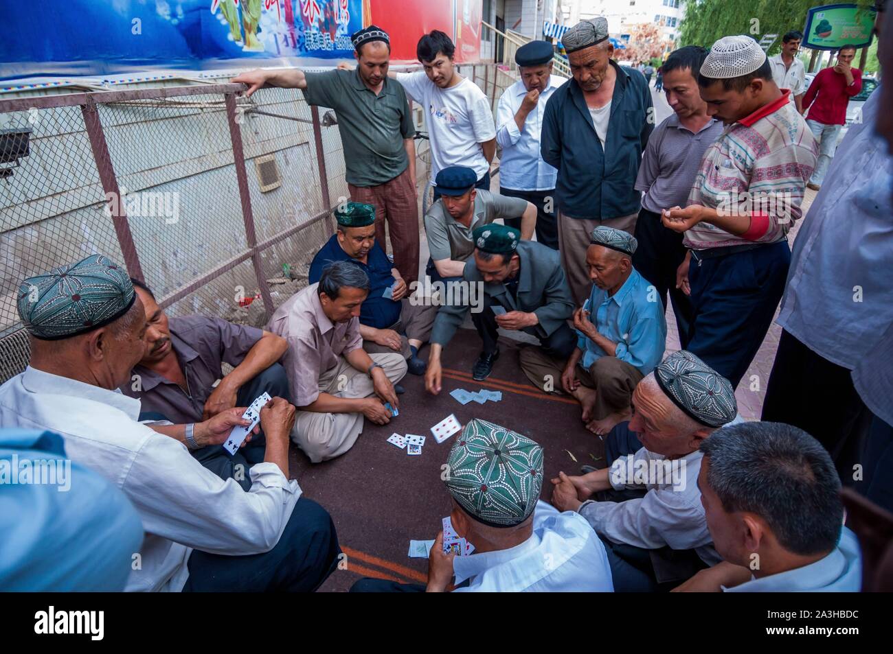 Cina, Xinjiang regione autonoma, Kashgar, Uiguri uomini giocando a carte in strada Foto Stock