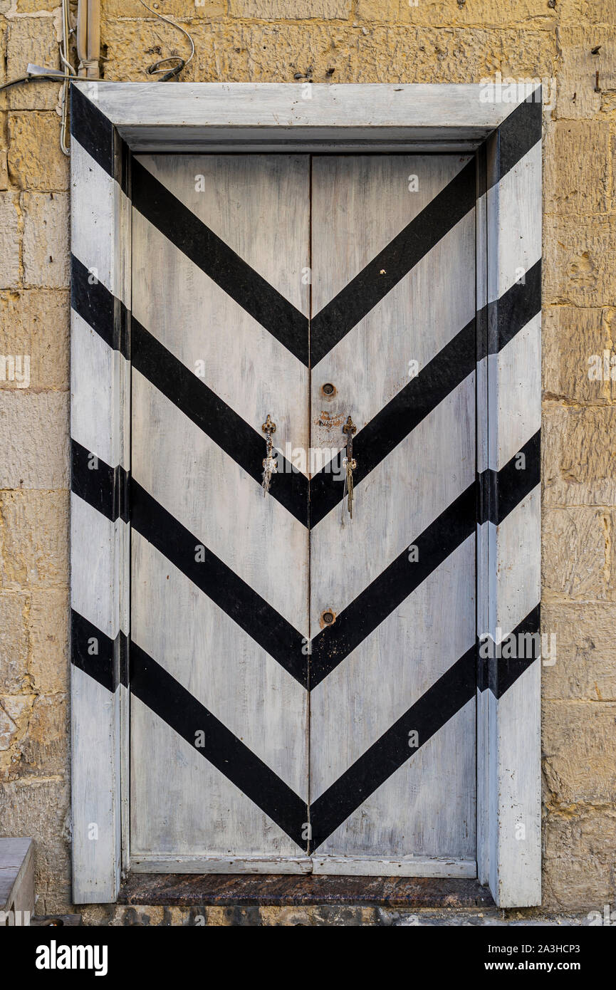 In bianco e nero di strisce diagonali dipinta su una vecchia porta di legno, Malta. Foto Stock