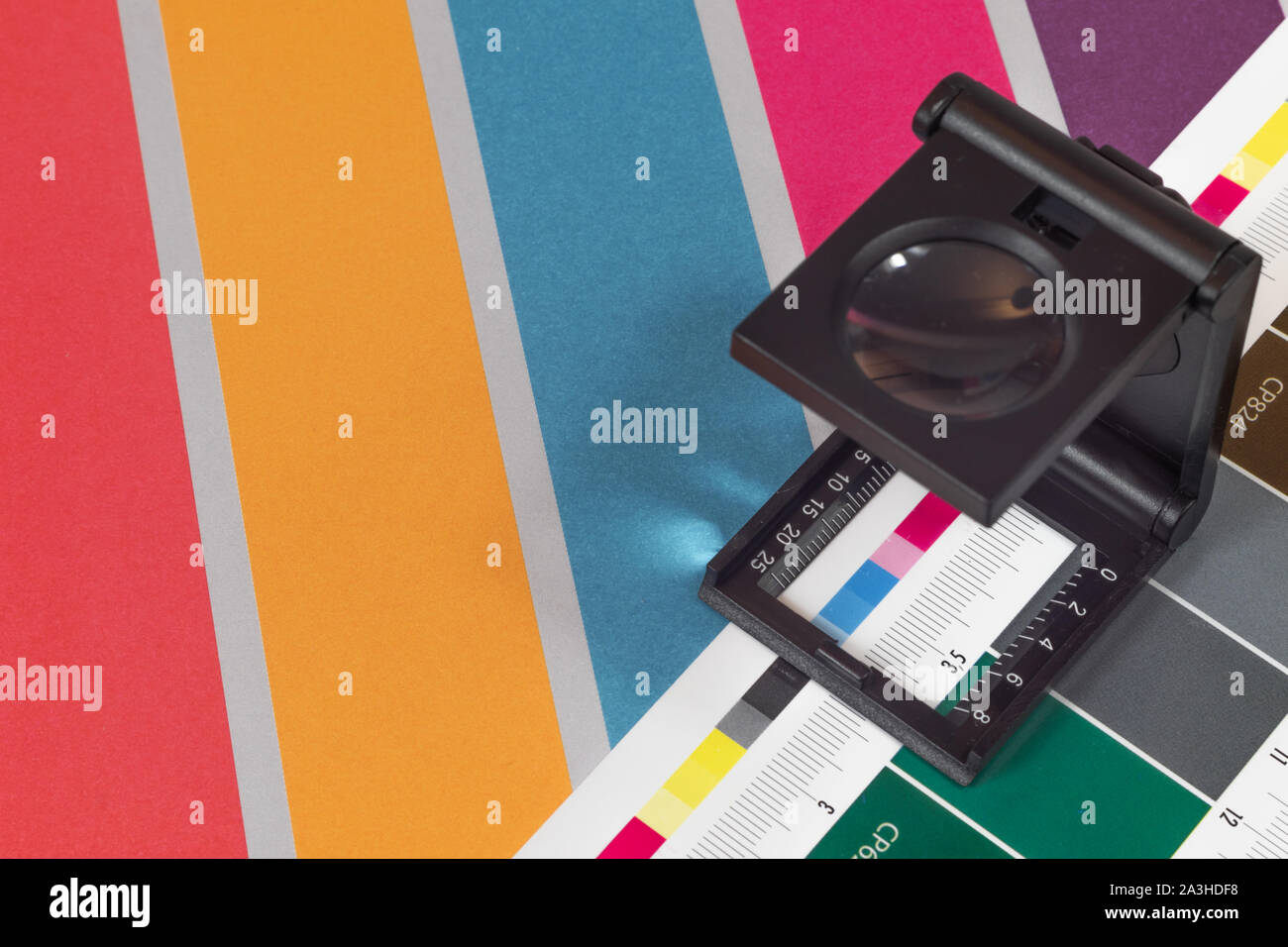 Nero lente di ingrandimento permanente sulla stampa di prova con sfondo colorato. Loupe stampa offset a foglio stampato con i colori di base barre di controllo. Foto Stock