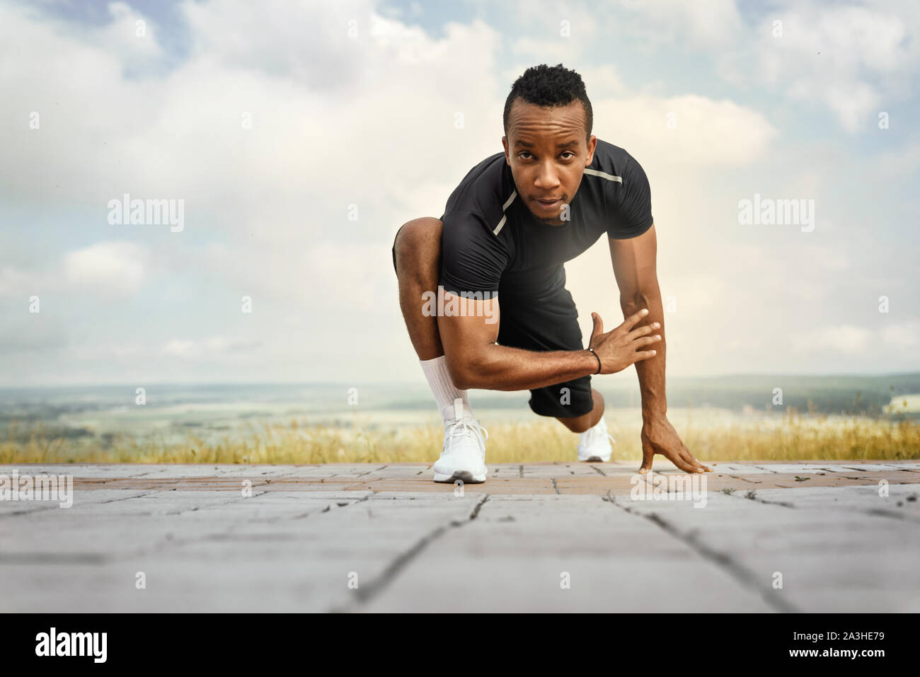 Bello atleta facendo esercizi di stretching. Uomo con corpo sportivo indossando in nero di t-shirt e shorts formazione in mattina. Sportivo in posa all'aperto, guardando la fotocamera. Foto Stock