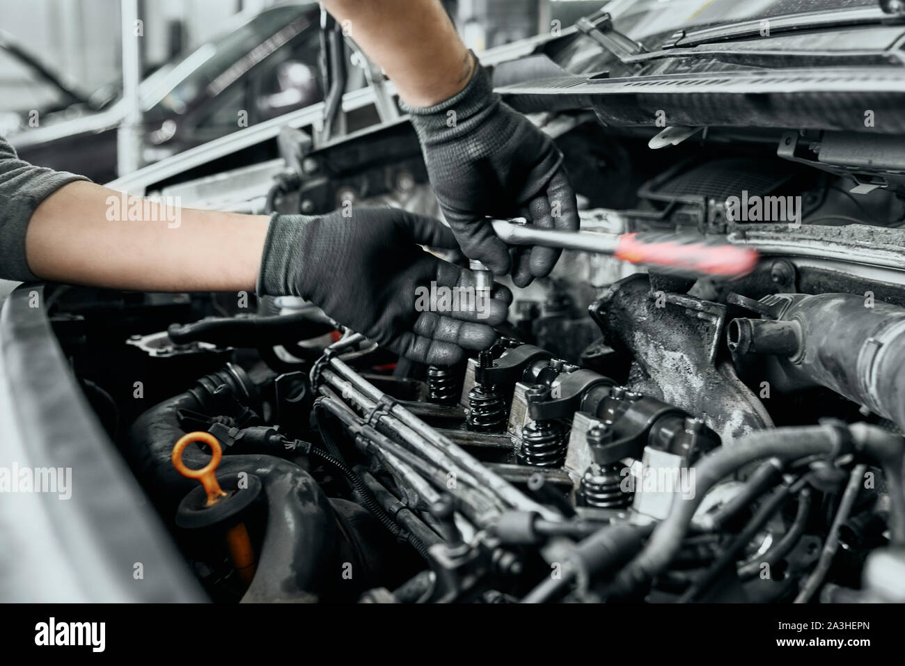 Uomo qualificati in nero guanti sporchi svita vecchie candele da auto a motore con una chiave per cambiarli in quelle nuove.Auto meccanico efficiente svolge le proprie funzioni di base nel centro di servizio Foto Stock