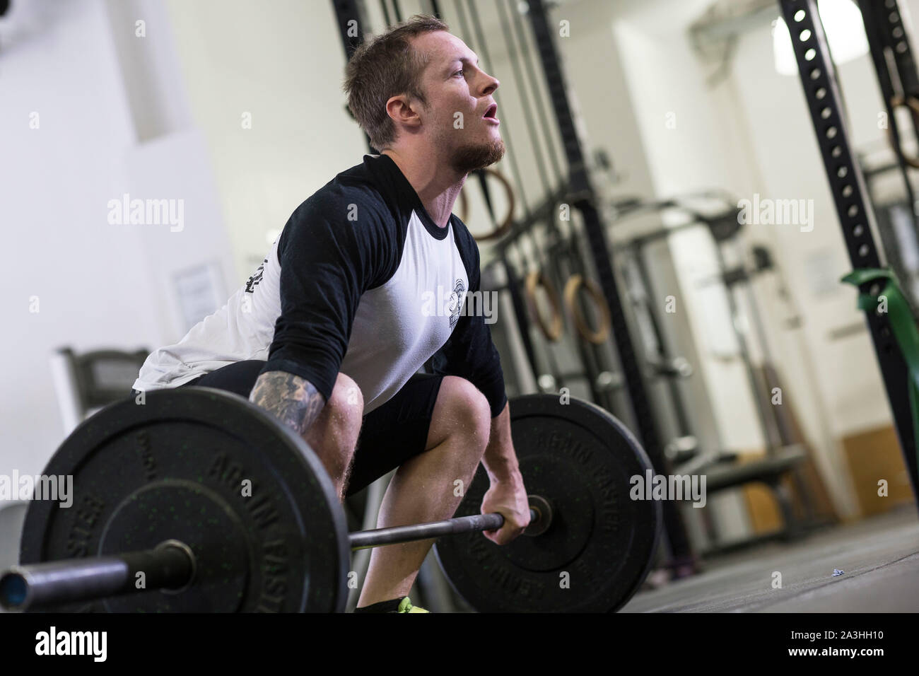 Un bianco giovane atleta maschio esegue diversi impianti di risalita e il peso corporeo dei movimenti in un ambiente palestra. Foto Stock