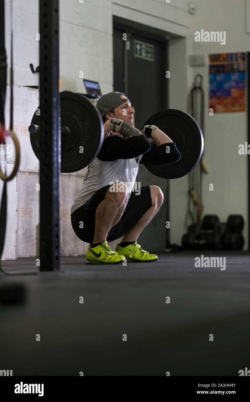 Un bianco giovane atleta maschio esegue diversi impianti di risalita e il peso corporeo dei movimenti in un ambiente palestra. Foto Stock