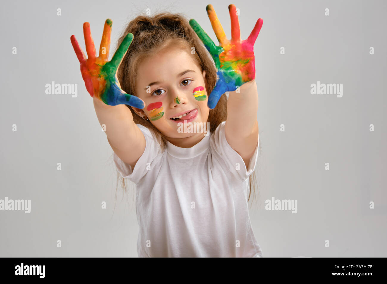 Bambina in t-shirt bianco è in posa in piedi isolato su bianco e mostrando il suo dipinto le mani, il viso. Studio d'arte. Close-up. Foto Stock