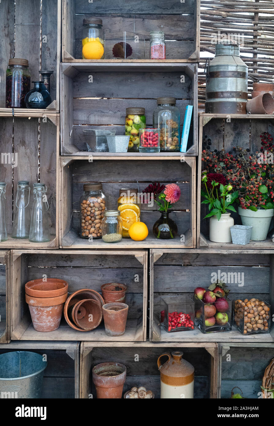 Vasetti di gin vecchio stile in forno infusi con frutta e noci con vasi di fiori recisi in un'esposizione di cassa di legno. REGNO UNITO Foto Stock