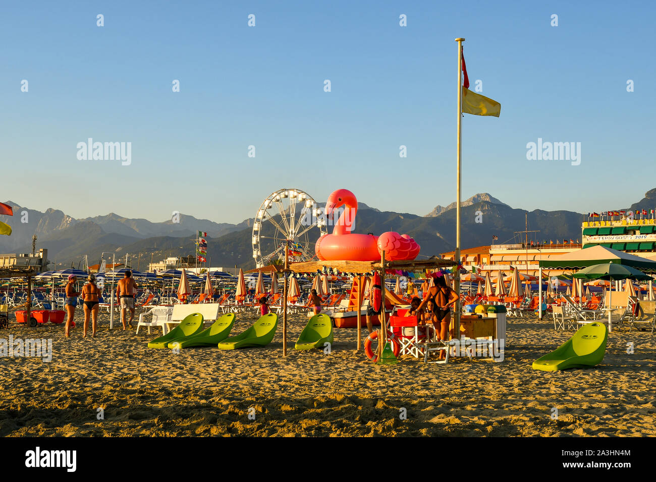 Vista panoramica della spiaggia sabbiosa di Lido di Camaiore con una rosa fenicottero gonfiabili, moderne sedie a sdraio sulla spiaggia e una ruota panoramica, Toscana, Italia Foto Stock
