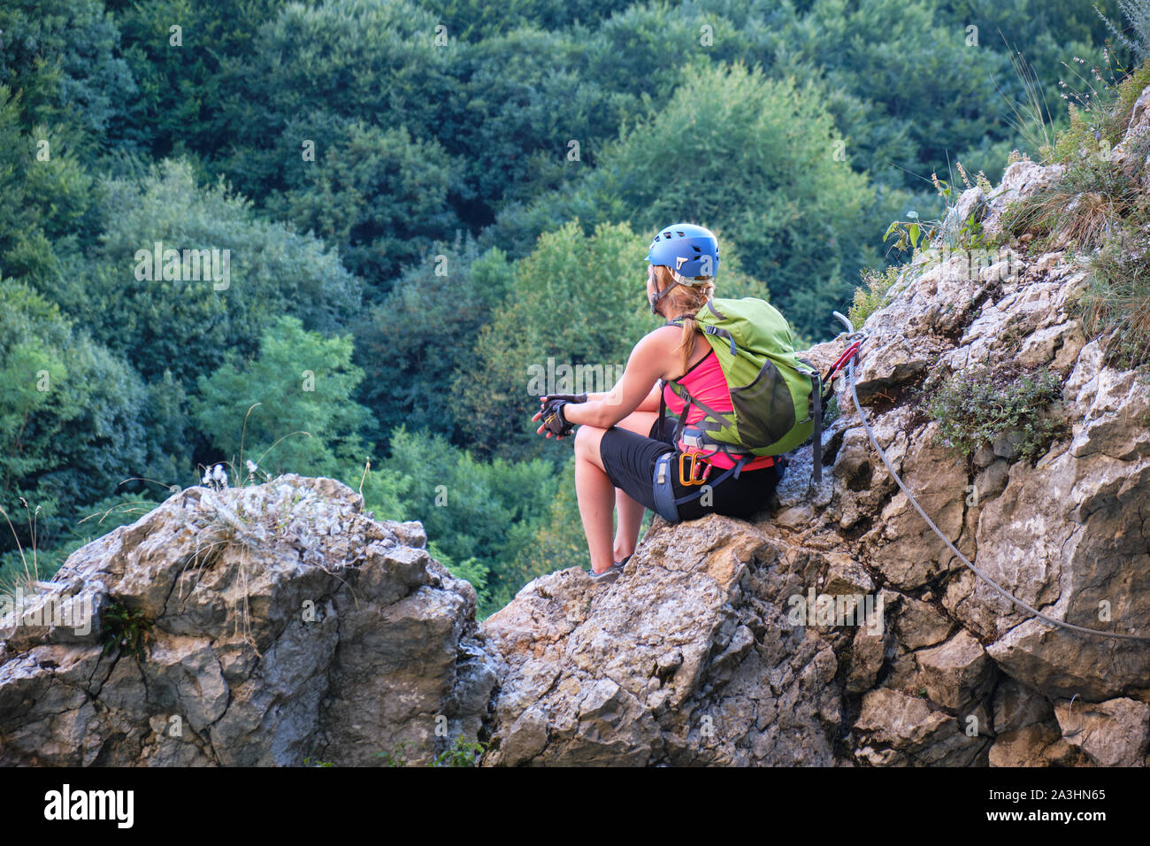 Donna seduta su rocce e ammirando la vista dalla Casa Zmeului via ferrata in Padurea Craiului mountains, Romania, al fianco di Crisul Repede river Foto Stock