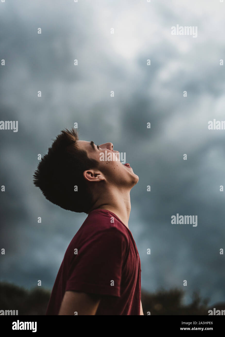 Teen boy guardando il cielo nuvoloso scuro con la sua bocca spalancata. Foto Stock