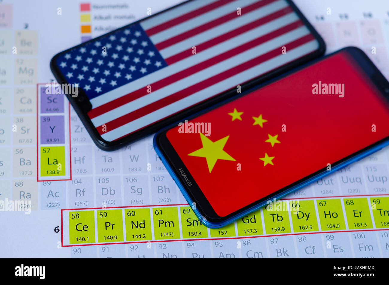 La foto di USA e Cina i flag su smartphone Huawei che si posa sulla tavola periodica attorno ai gruppi di terre rare minerali. Concettuale. Foto Stock