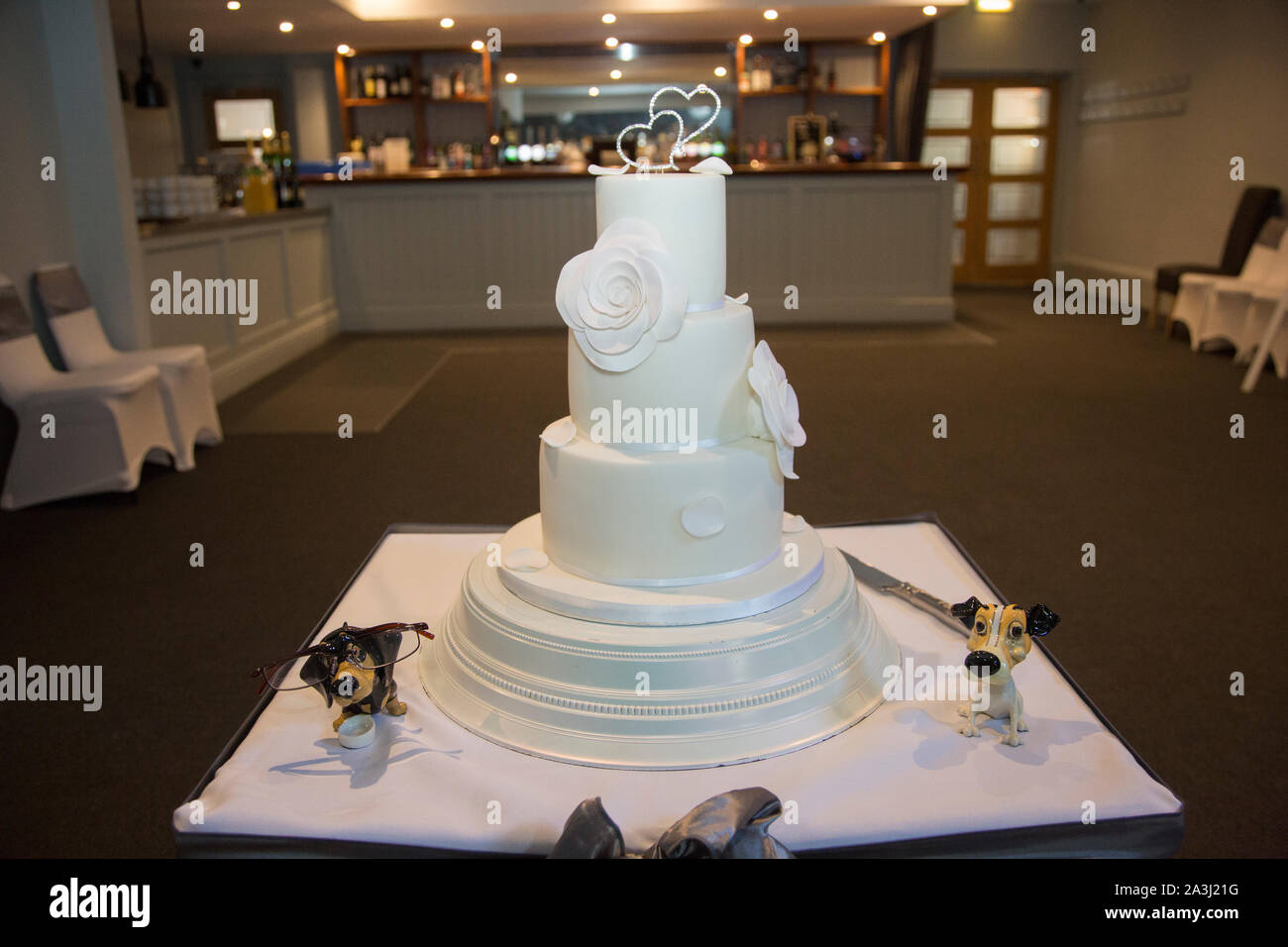 Tiered, ghiaccio, torta di nozze su una torta decorata stand pronto per essere tagliato con la sposa e lo sposo presso il ricevimento di nozze Foto Stock
