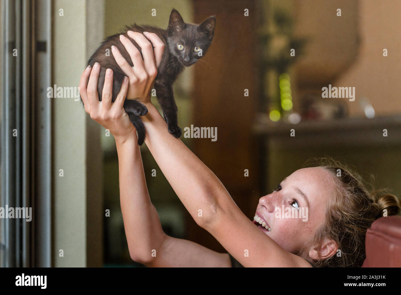 Teen ragazza sorride come ella ascensori minuscoli gattino nero in aria in alto Foto Stock