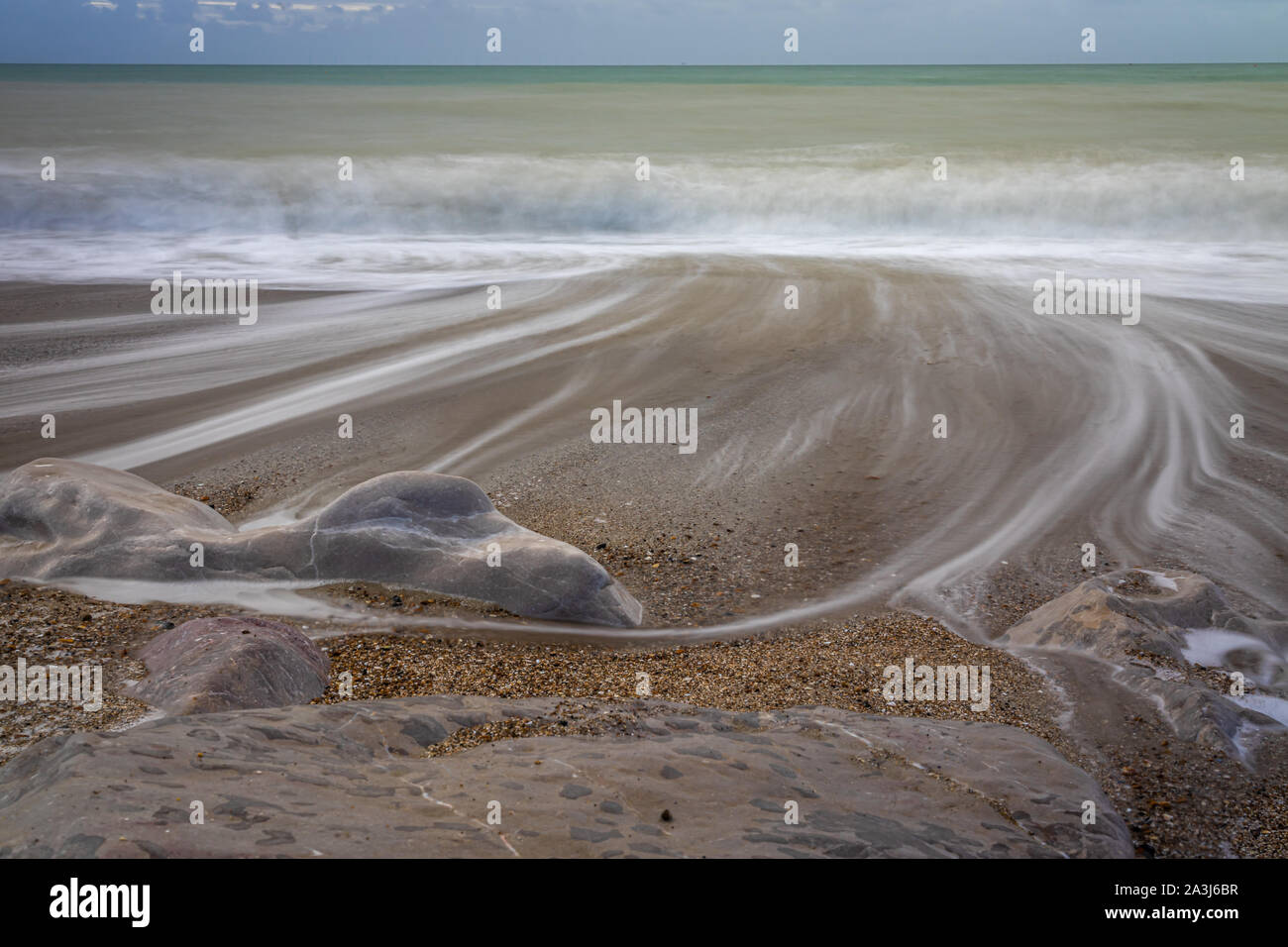 Ritirandosi onde sulla spiaggia ghiaiosa Foto Stock