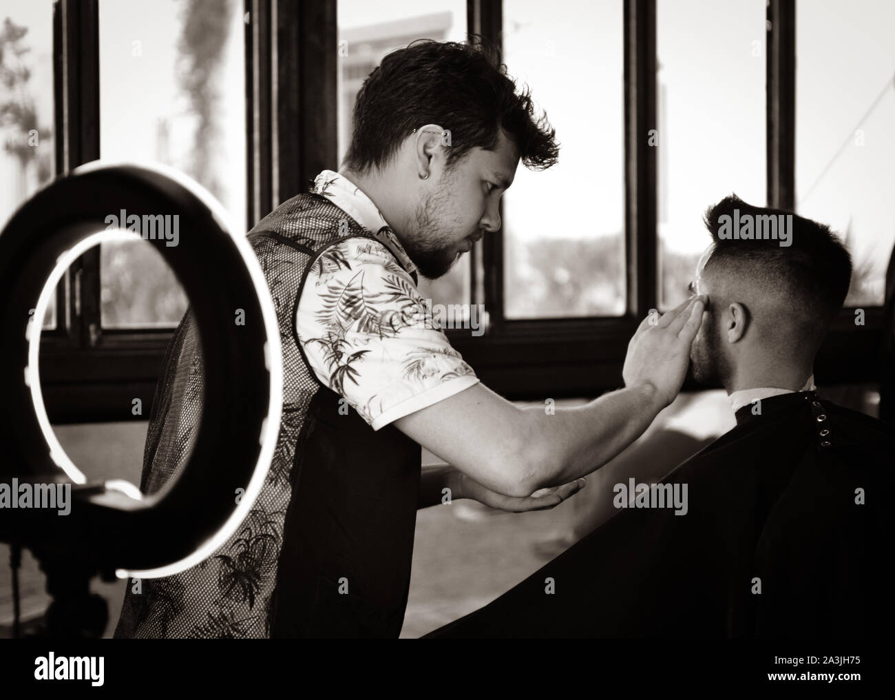 Dopo un nuovo taglio di capelli, barbiere preps un client per una rasatura con l aiuto di una moderna luce ad anello a '81 Barbieri in Tucson, AZ, Stati Uniti d'America Foto Stock