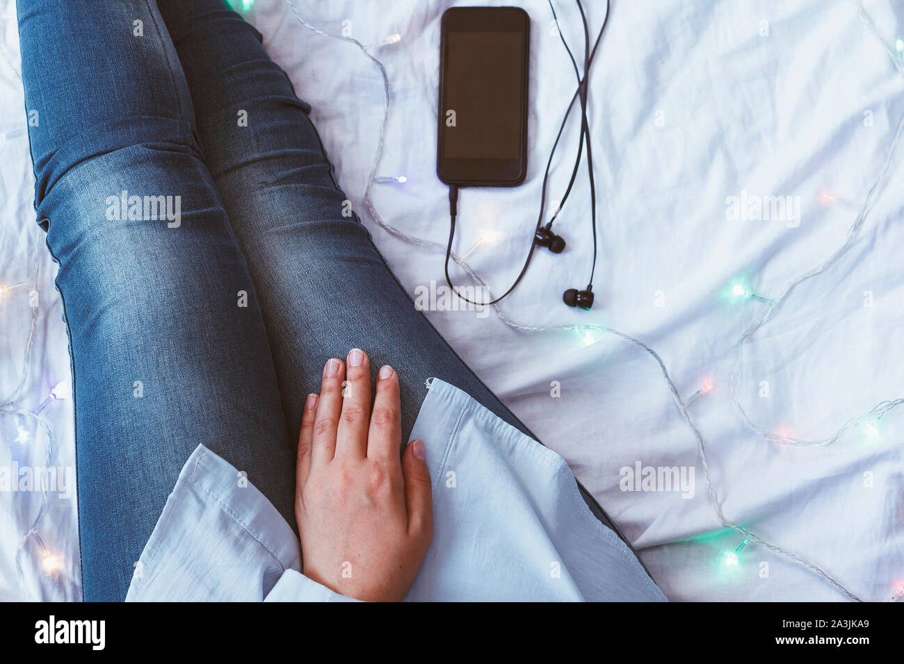 Una donna cerca di dormire dopo una dura giornata di lavoro. Rilassante  femmina in una accogliente camera da letto. Ascolto di musica su uno  smartphone. In autunno o inverno Foto stock -